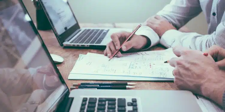 person holding pencil near laptop computer